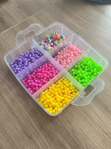 A plastic container with six compartments. Brightly coloured beads in each compartment.