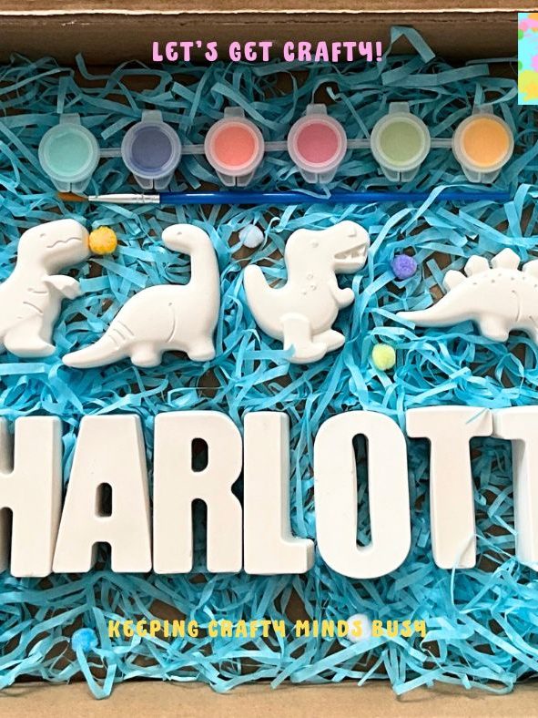 Three dinosaurs on top of blue tissue paper, six paints, paintbrush and plaster of Paris name.