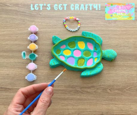 A child holding a paintbrush painting a large plaster of Paris turtle. A bracelet in brightly coloured beads at the top of the picture.