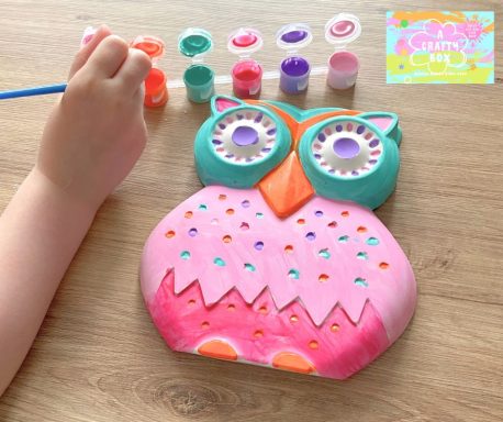 A child holding a paintbrush painting a large owl in bright colours.